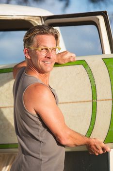 Single adult handsome man pulling surfboard out of his van