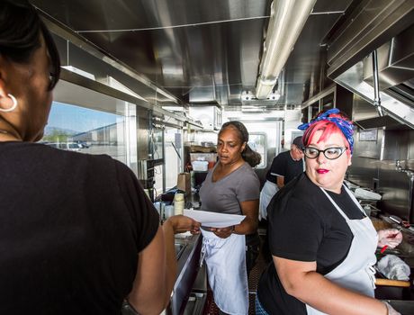 Female chef with pink hair works alongside crew on food truck