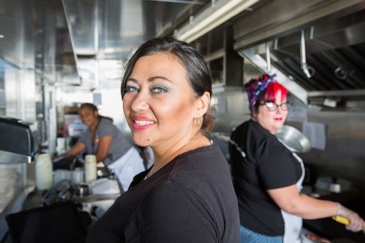 Three busy workers inside food truck preparing a meal