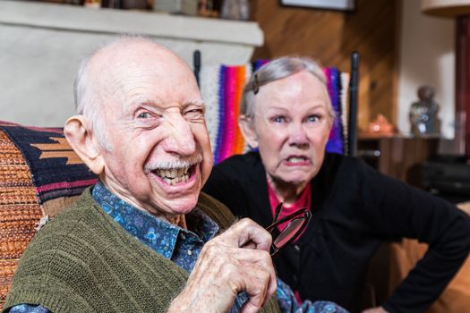 Angry old couple sitting indoors with scowling expression
