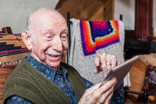 Smiling older gentleman working on a tablet in his living-room