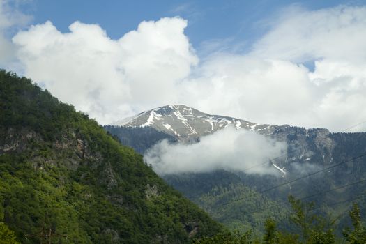 Mountains are covered with snow and the wood and surrounded with clouds