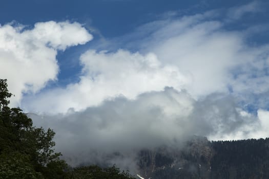 Mountains are covered with snow and the wood and surrounded with clouds