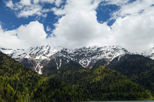 Mountains are covered with snow and the wood and surrounded with clouds