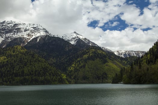 Mountains are covered with snow and the wood and surrounded with clouds