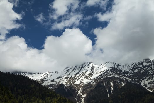 Mountains are covered with snow and the wood and surrounded with clouds