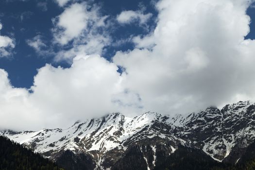 Mountains are covered with snow and the wood and surrounded with clouds