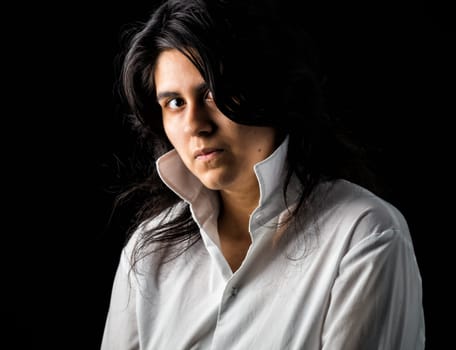 Latina teen in white shirt standing in front of black backdrop and looking at the camera