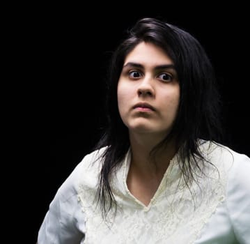 Latina teenager in white standing in front of a black background with an angry, suspicious, serious look on her face.