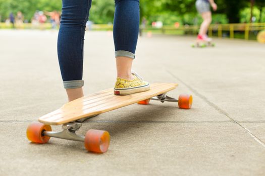 Teenage girl wearing blue jeans and sneakers practicing long board riding in skateboarding park. Active urban life. Urban subculture.