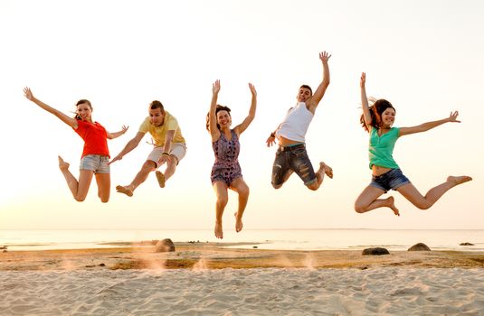 friendship, summer vacation, holidays, party and people concept - group of smiling friends dancing and jumping on beach