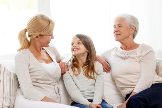 family, happiness, generation and people concept - smiling mother, daughter and grandmother sitting on couch at home