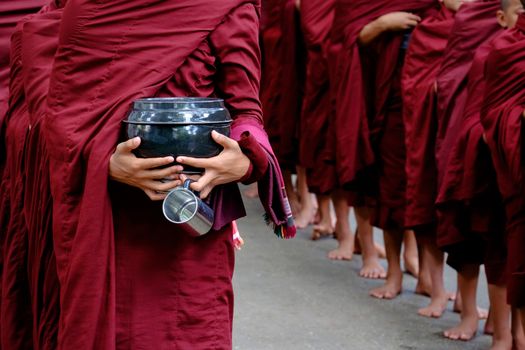 Detail of buddhist monks crowd in red robes and person holding a bowl and cup