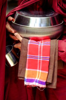 Close up of buddhist monk in a robe and his hands holding a bowl and cup