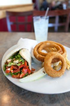 Chicken pita wrap sandwich with onion rings and a deli pickle slice. Shallow depth of field.