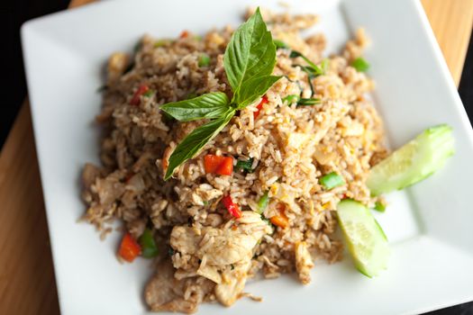 A Thai dish of chicken fried rice presented on a square white plate.  Shallow depth of field.
