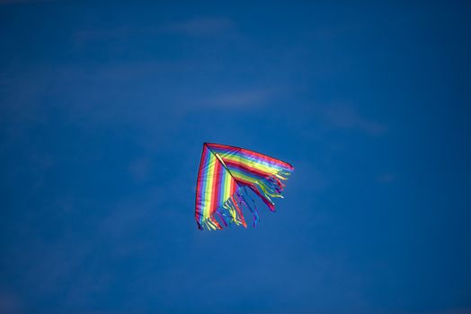 A bridht colored kite flying high against a blue sky