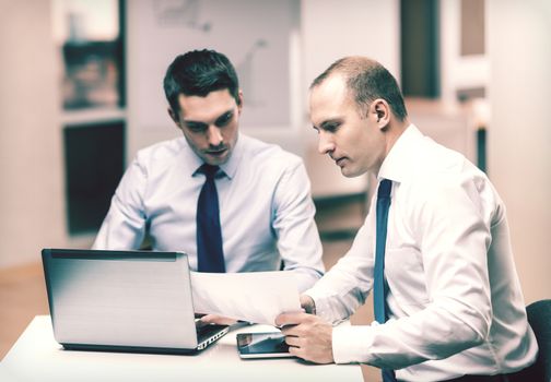 business, technology and office concept - two businessmen with laptop, tablet pc computer and papers having discussion in office