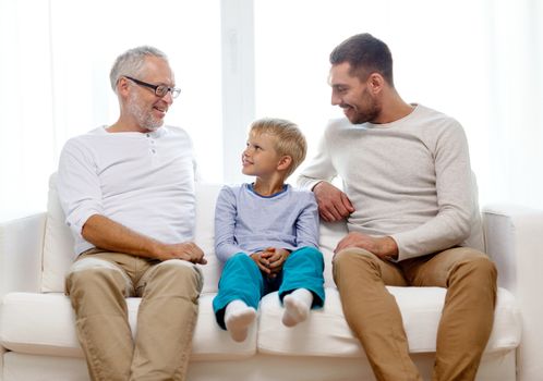 family, happiness, generation and people concept - smiling father, son and grandfather sitting on couch at home