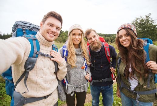 adventure, travel, tourism, hike and people concept - group of smiling friends with backpacks making selfie outdoors