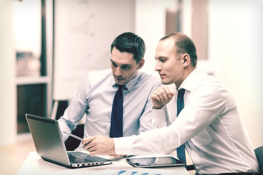 business, technology and office concept - two businessmen with laptop, tablet pc computer and papers having discussion in office