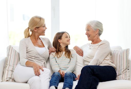 family, happiness, generation and people concept - smiling mother, daughter and grandmother sitting on couch at home