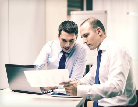 business, technology and office concept - two businessmen with laptop, tablet pc computer and papers having discussion in office