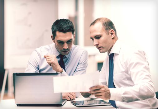 business, technology and office concept - two businessmen with laptop, tablet pc computer and papers having discussion in office