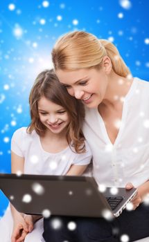 family, childhood, holidays, technology and people concept - smiling mother and little girl with laptop computer over blue snowy background