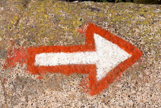 Red and white arrow painted on a rock of mountain. Hiking trail sign symbol in Italy alps