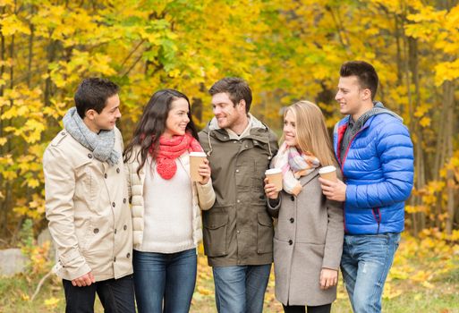 love, relationship, season, friendship and people concept - group of smiling men and women walking with paper coffee cups in autumn park