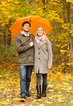 love, relationship, season, family and people concept - smiling couple with umbrella walking in autumn park