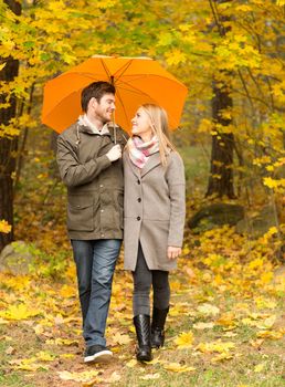 love, relationship, season, family and people concept - smiling couple with umbrella walking in autumn park