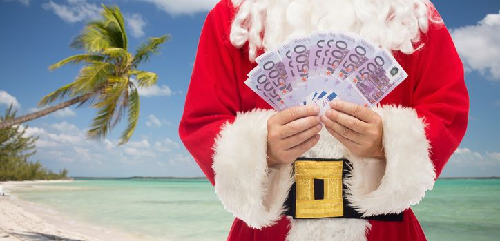 christmas holidays, winning, currency, travel and people concept - close up of santa claus with euro money over tropical beach background