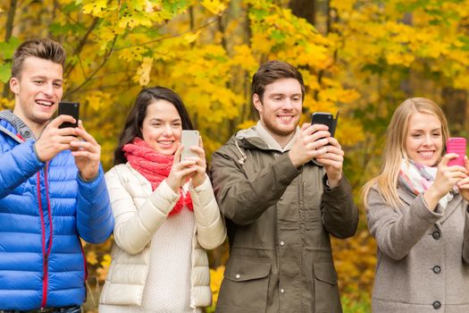 season, people, technology and friendship concept - group of smiling friends with smartphones taking picture in autumn park