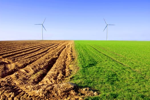 Windmills on the field conceptual image. Windmills on the plowed and green field.