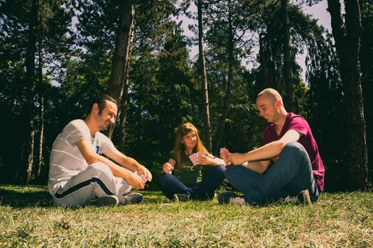 Three friend having fun by playing cards in the forest