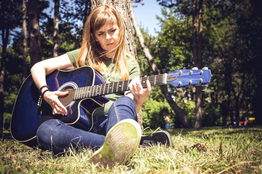 Girl singing to a guitar surrounded by trees in a park