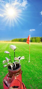 Golf game. Golf clubs in bag against the golf course with bright sun.