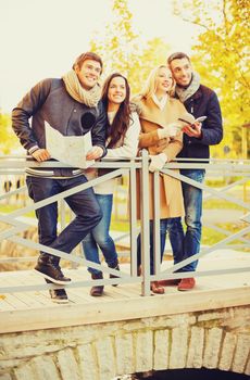 holidays and tourism concept - group of friends or couples with tourist map in autumn park