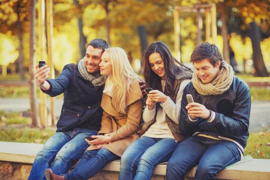 summer, holidays, vacation, happy people concept - group of friends or couples with smartphone having fun in autumn park