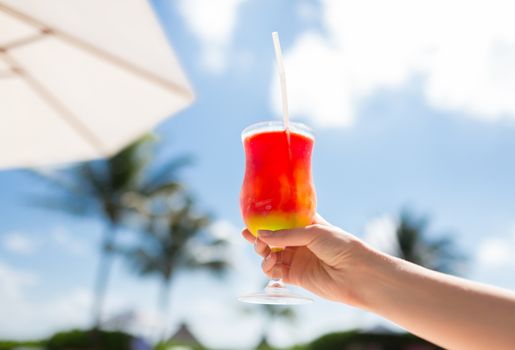 vacation, beverage and travel concept - close-up of female hand holding glass with cocktail