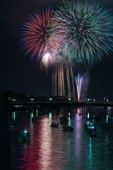 Colorful fireworks reflected in a river with many small boats and a cityscape along the side in the countryside of Kochi, Japan.
