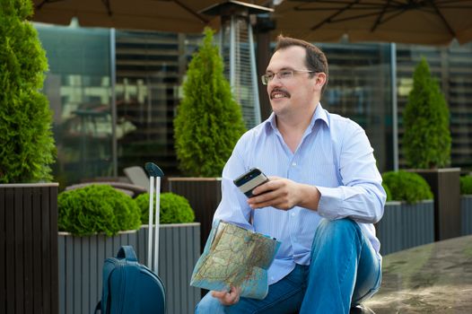 Traveler with mobile phone and city plan sitting outdoors.