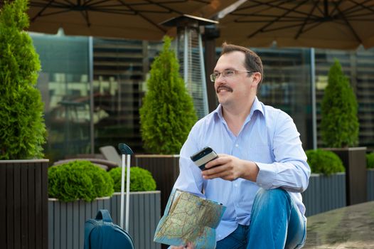 Traveler with mobile phone and city plan sitting outdoors.