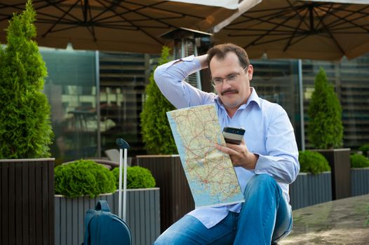 Traveler with mobile phone and city plan sitting outdoors.