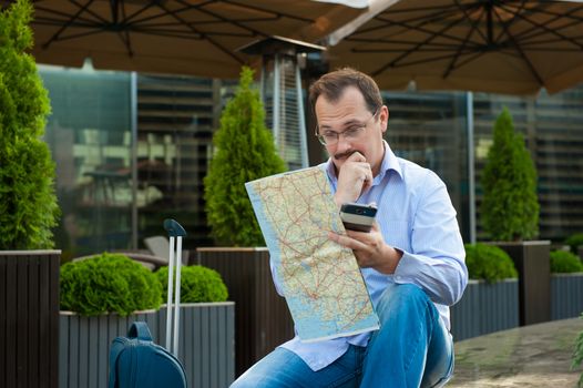 Traveler with mobile phone and city plan sitting outdoors.