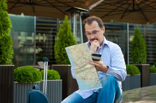 Traveler with mobile phone and city plan sitting outdoors.