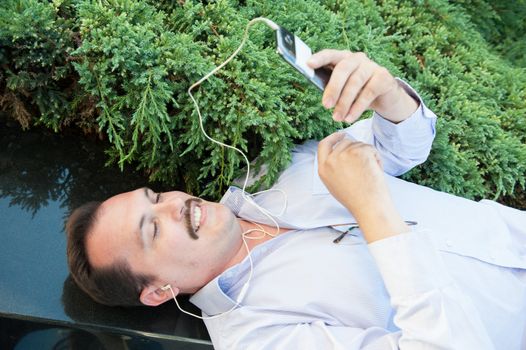 Urban man using smart phone outside using app on 4g wireless device wearing headphones. Lying on the Marble fence