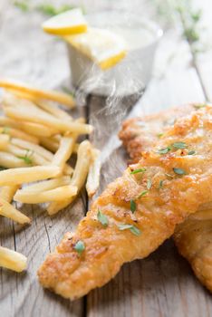 Fish and chips. Fried fish fillet with french fries on wooden background. Fresh cooked with hot steams.